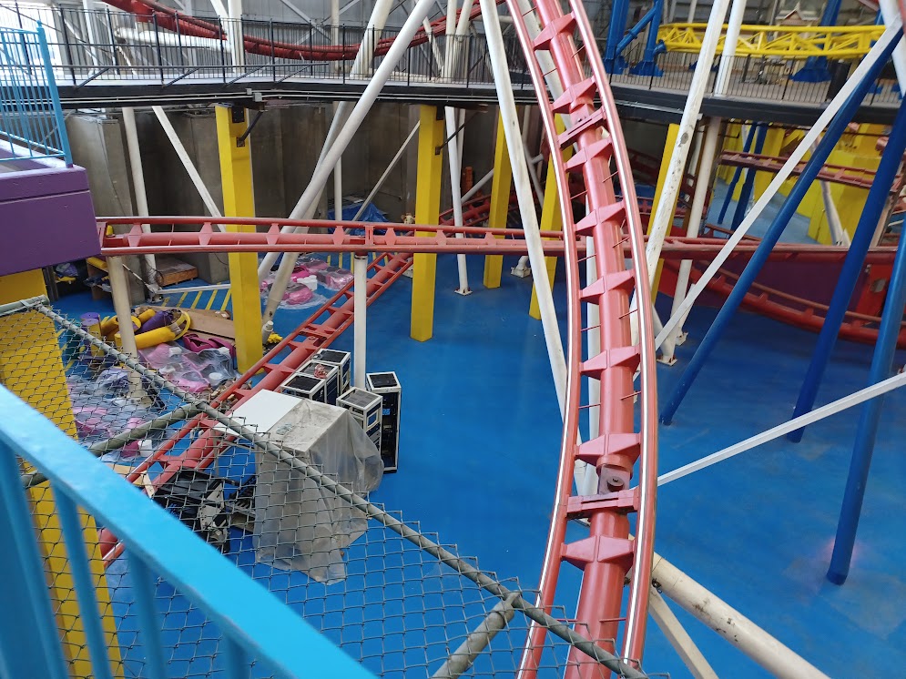 A photo of the Mindbender's lower section, with one of the tracks disappearing beneath the catwalk the photographer's standing on. There are some items being held as storage on the ground.