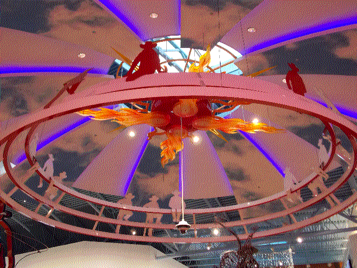 A ceiling display of a flaming sun, with painted clouds on the ceiling and white rays with blue LED's. There's a ring around the sun, with cowboy cutouts sitting along the edge.