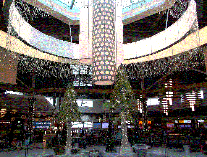 In the middle of the food court are more trees made out of christmas lights, above is a large lights display with white light dangling from it.